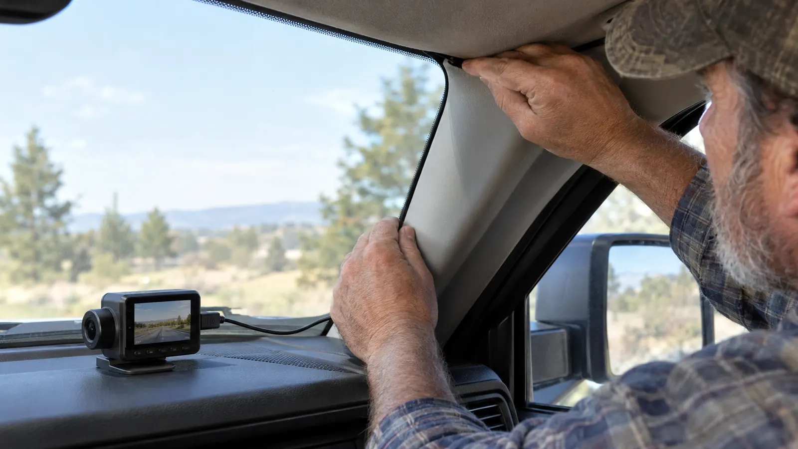 A hand routing a power cable along the edge of a windshield headliner in a pickup truck
